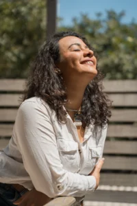 Débora Lucas sorrindo com os olhos fechados ao ar livre, simbolizando a leveza, a presença e a autonomia alcançadas nas sessões de terapia transpessoal.
